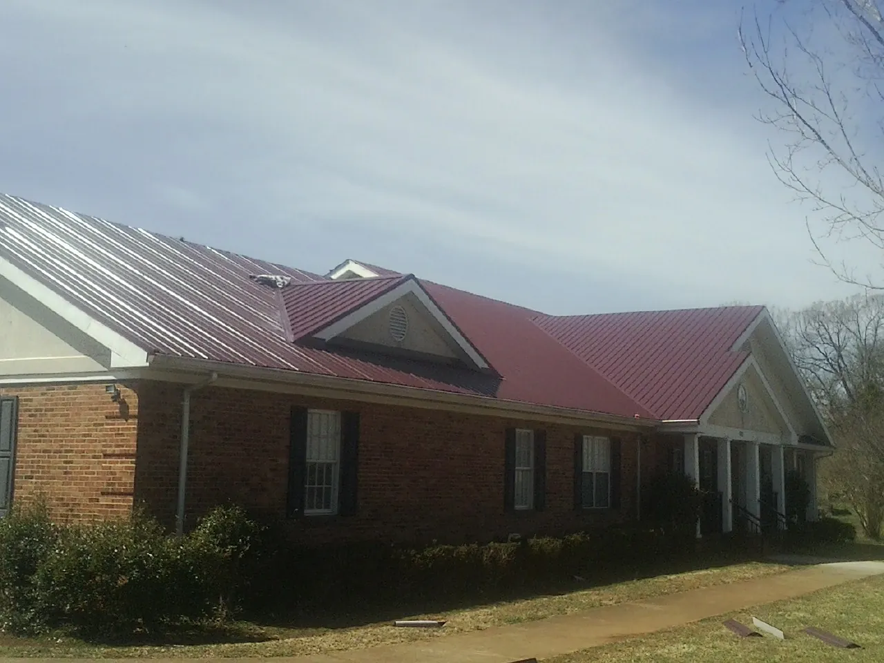 Red metal roof with gabled entries on a long brick building, from a Hail Damage Roof Repair job in Merrittstown
