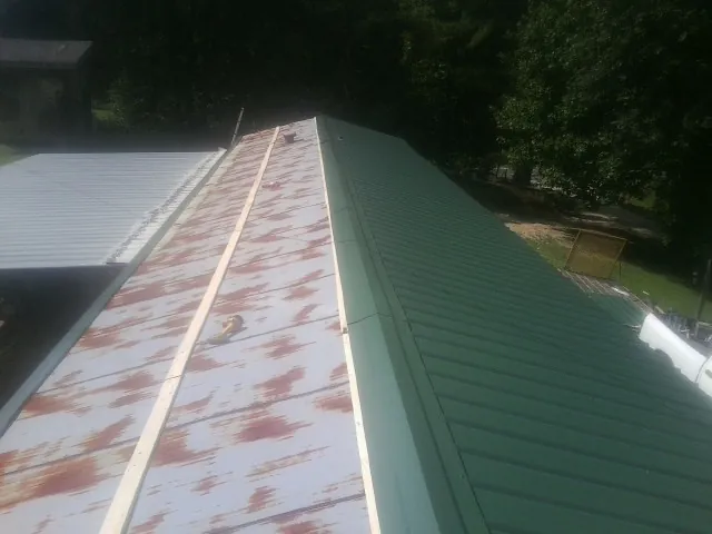 Old rusted panels beside newly installed green metal roofing — Wind Damage Roof Repair by Roofing Brothers in Merrittstown