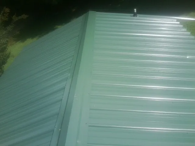 New green metal panels meeting at the ridge of a roof — Flat Roof Repair work by our crew in Merrittstown