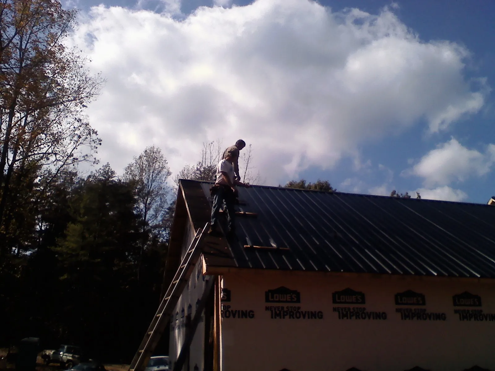 Roofer fastening dark metal panels high against a cloudy sky, from a Roof Inspection job in Merrittstown
