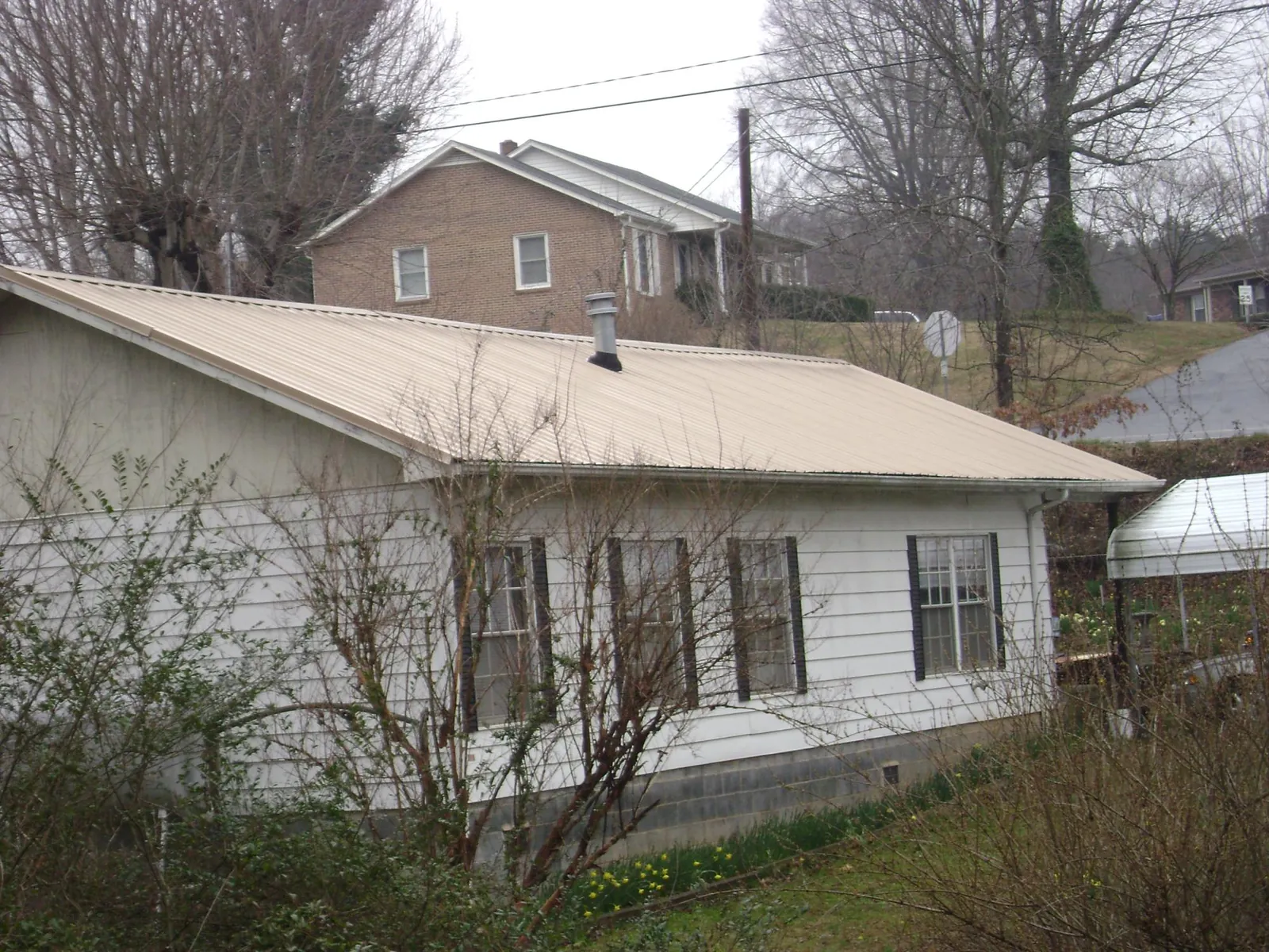 Tan metal roof on a white sided house set into a hillside — Commercial Roofing by Roofing Brothers in Merrittstown