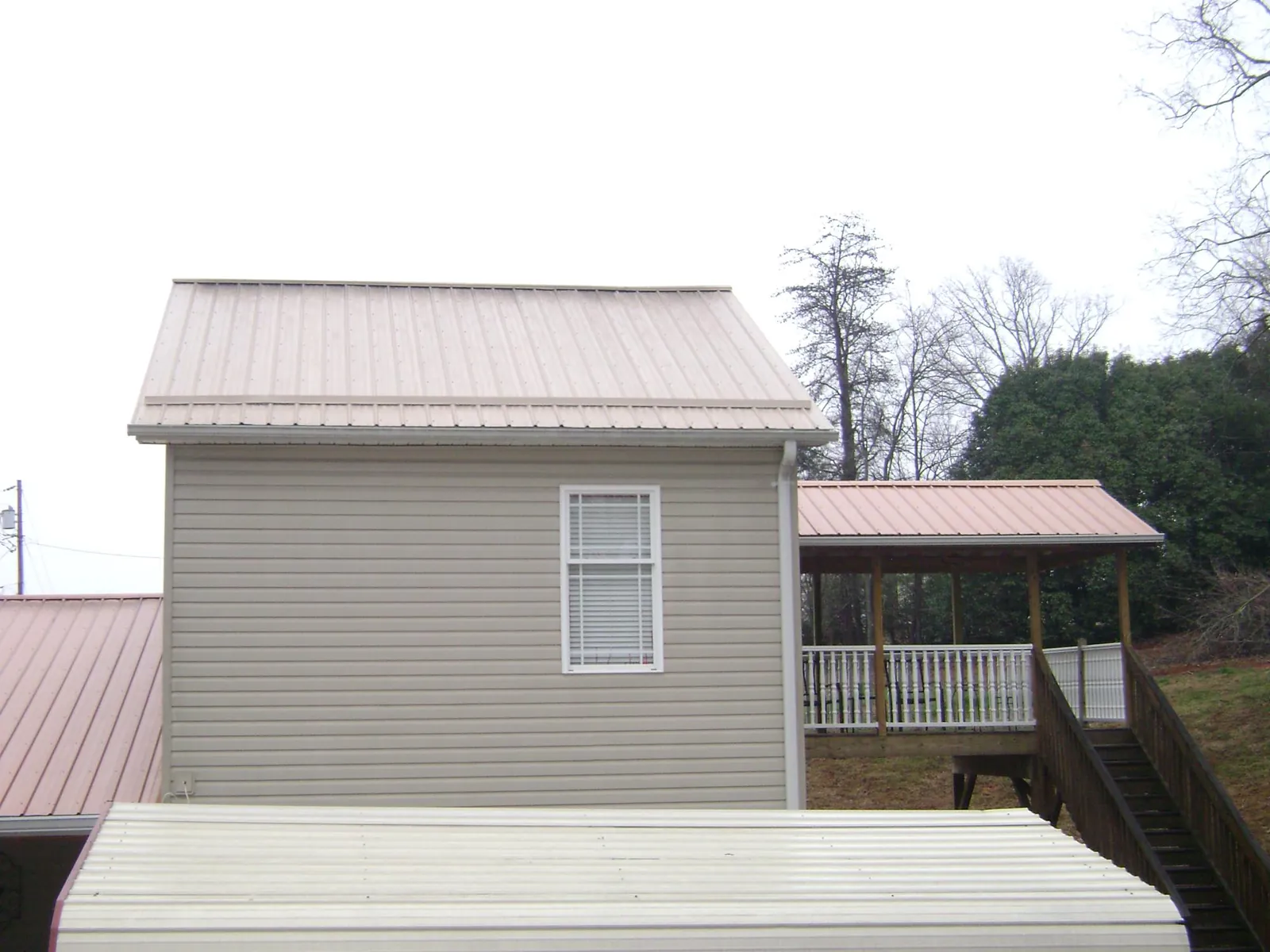 Tan metal roofs on a two story addition and attached porch, from a Roof Replacement job in Merrittstown